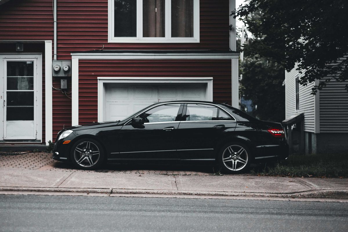 A black four-dour sedan parks in the driveway of a suburban house