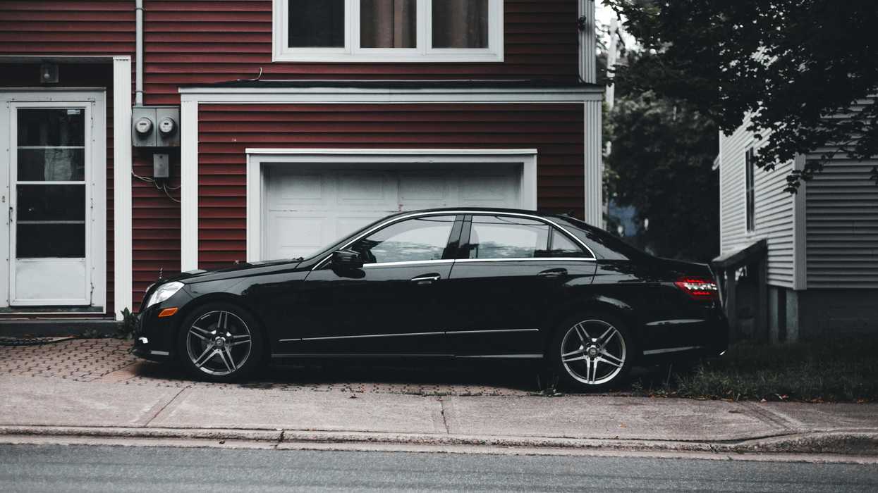A black four-dour sedan parks in the driveway of a suburban house