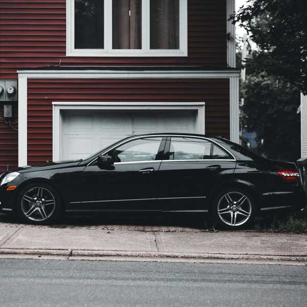 A black four-dour sedan parks in the driveway of a suburban house