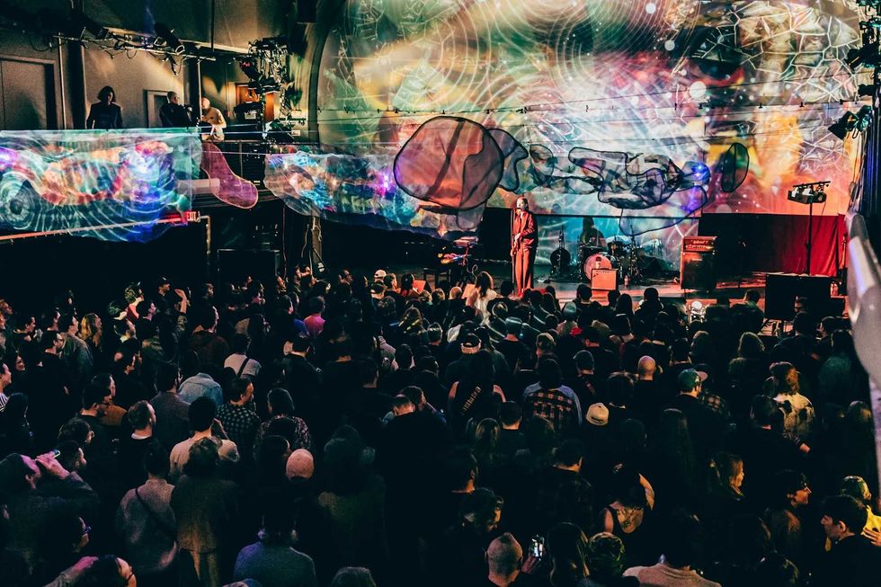 A crowd watches a performer on stage in a packed concert space.