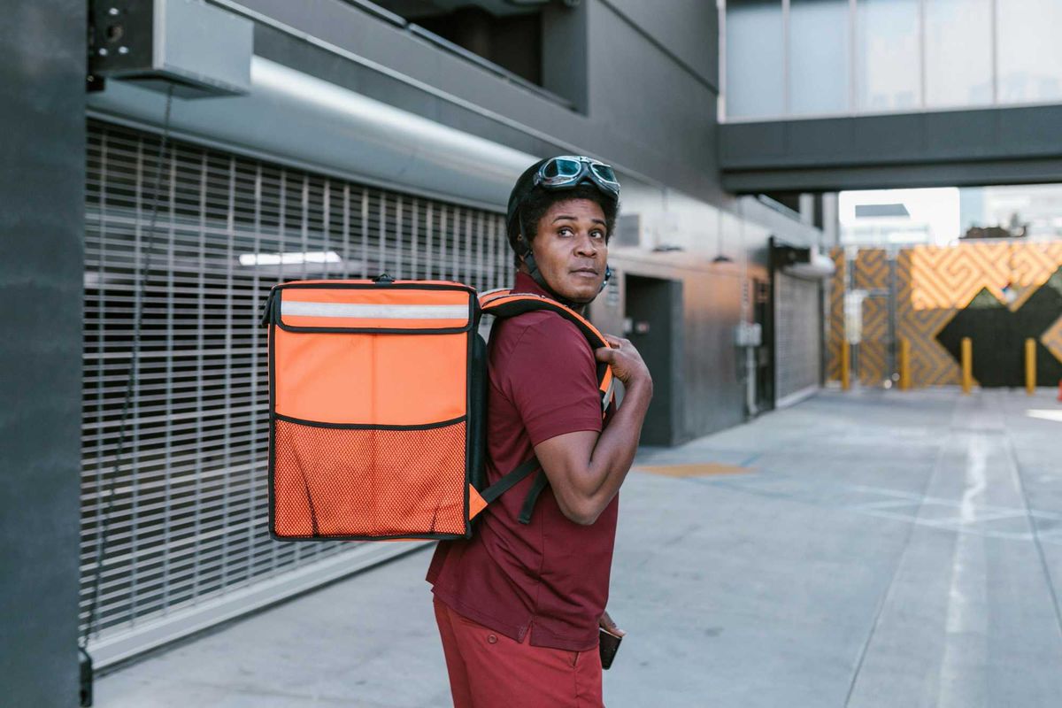 A delivery person carries a large food transportation bag on their back