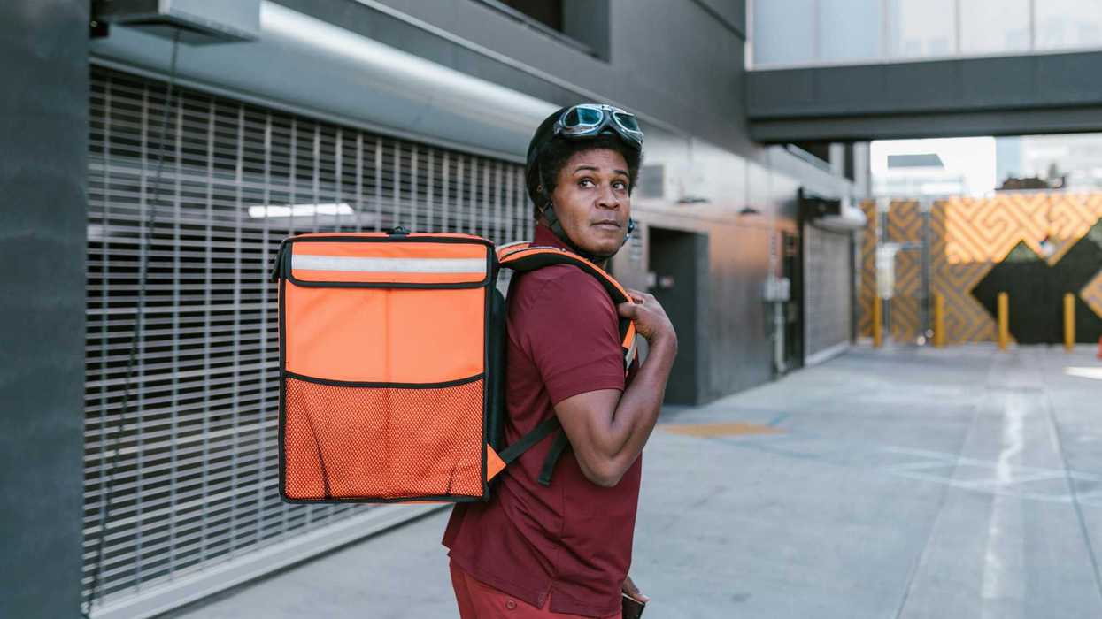 A delivery person carries a large food transportation bag on their back