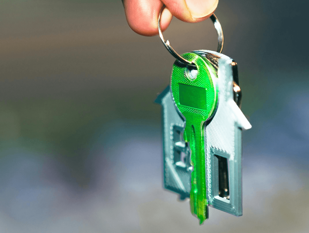 A hand holds a keyring with a bright green key and a house-shaped charm