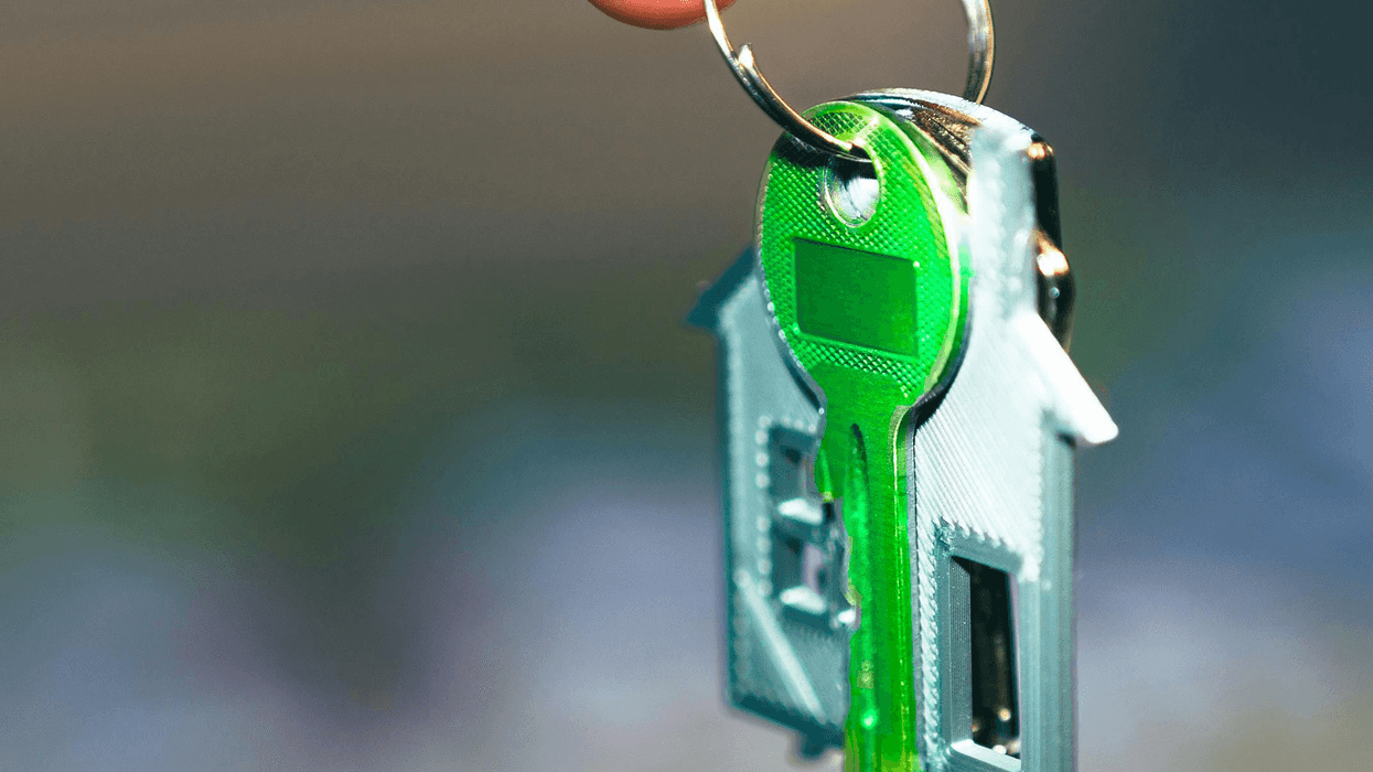 A hand holds a keyring with a bright green key and a house-shaped charm