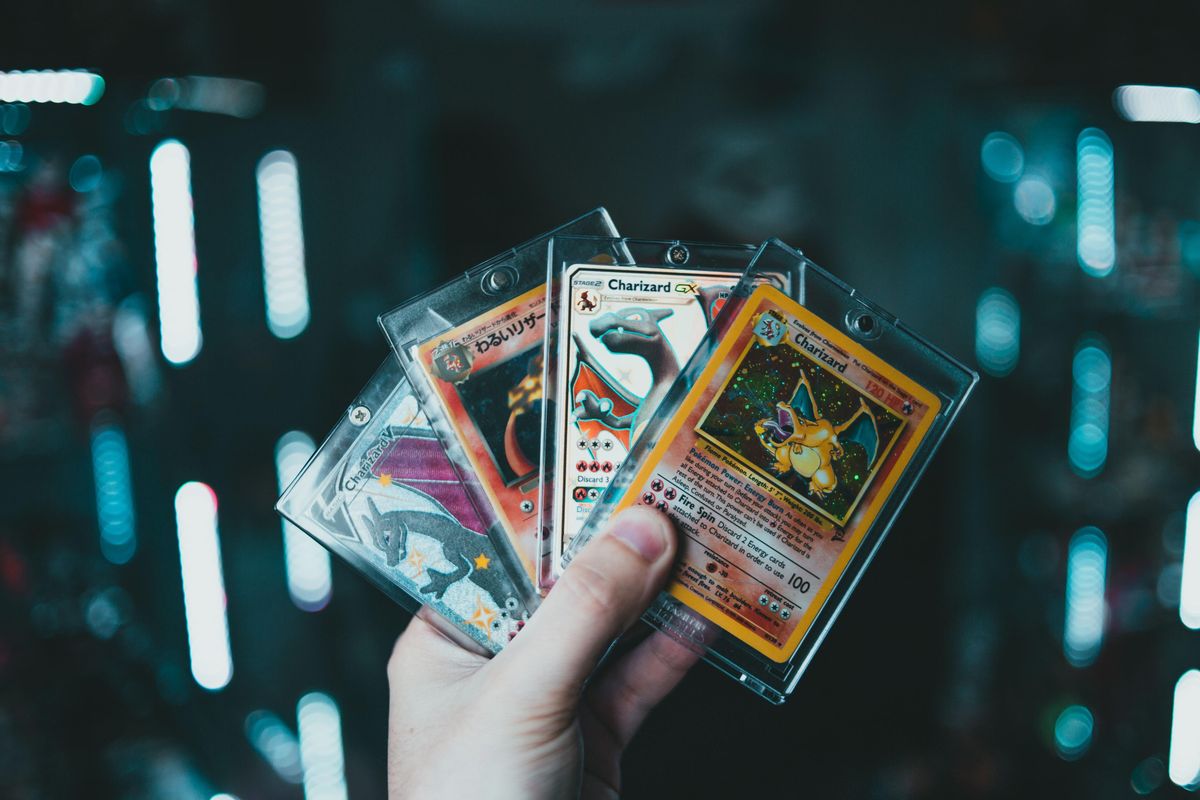 A hand holds four Pokémon cards fanned out.