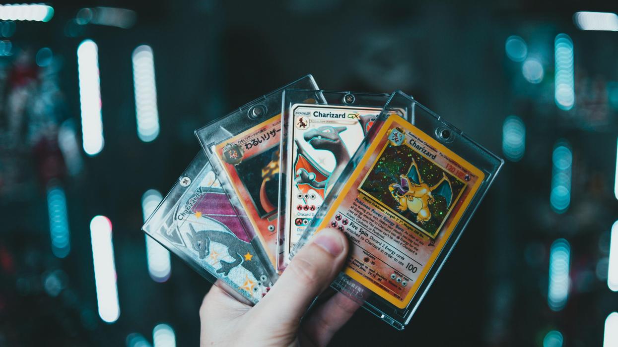 A hand holds four Pokémon cards fanned out.