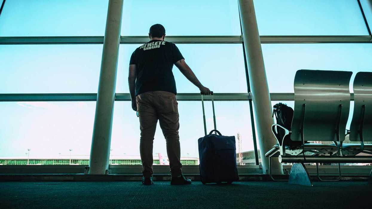 A man at the airport stares out the window at the airplanes