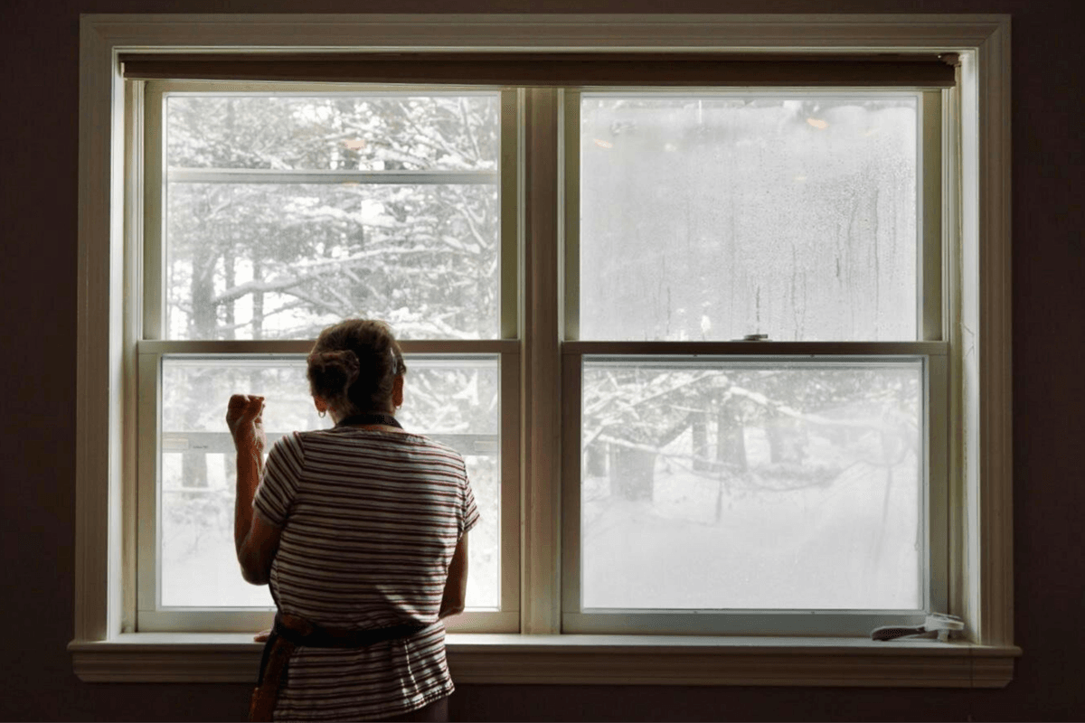 A person in an apron looks out the window at a lot of snow
