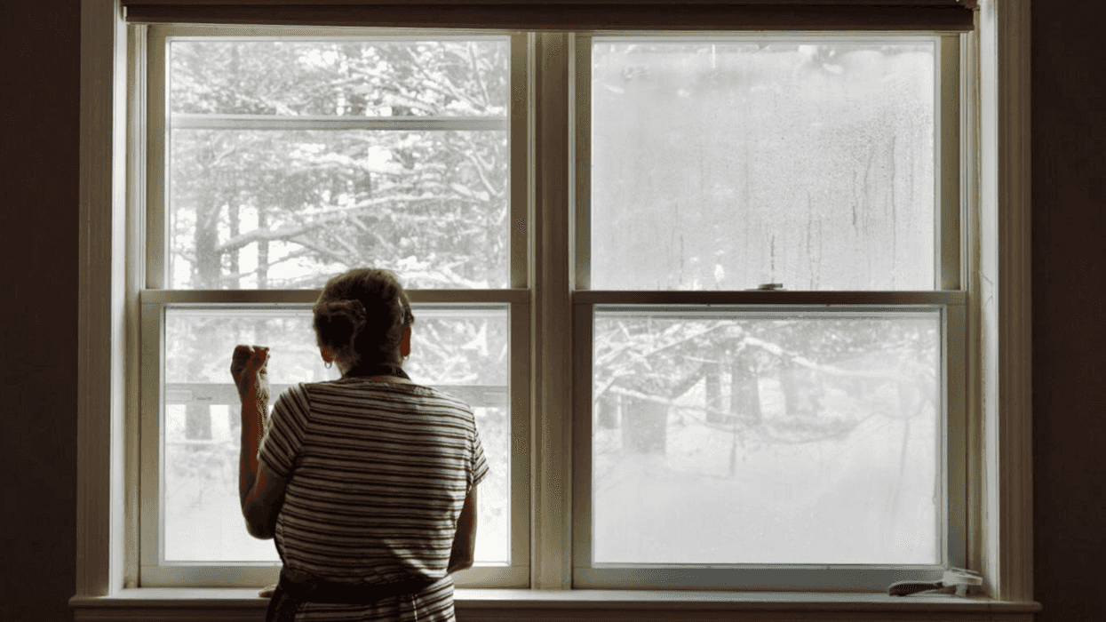 A person in an apron looks out the window at a lot of snow