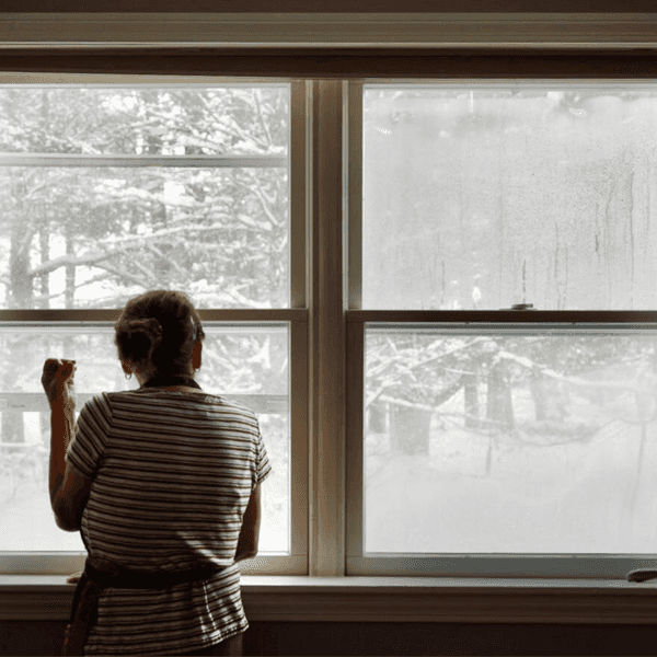 A person in an apron looks out the window at a lot of snow