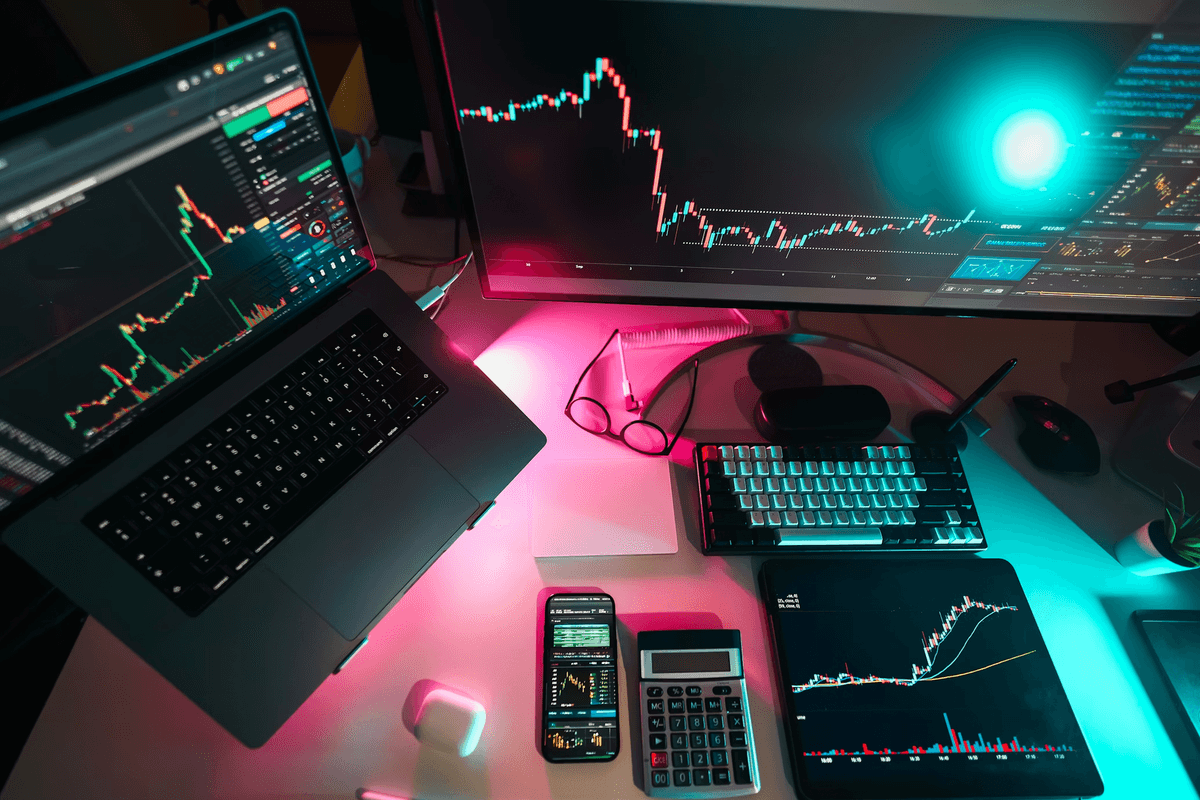A person's desk with a computer screen, laptop, tablet, and calculator as they research stocks