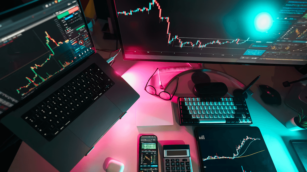 A person's desk with a computer screen, laptop, tablet, and calculator as they research stocks