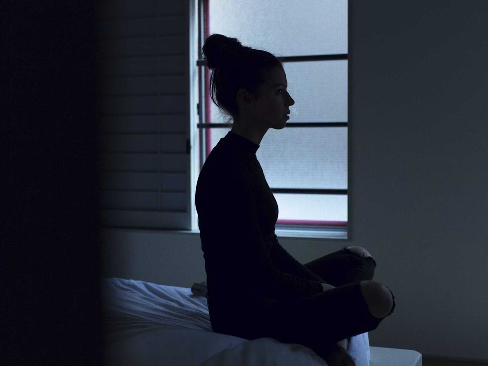 a woman sits cross-legged on a bed, staring into space