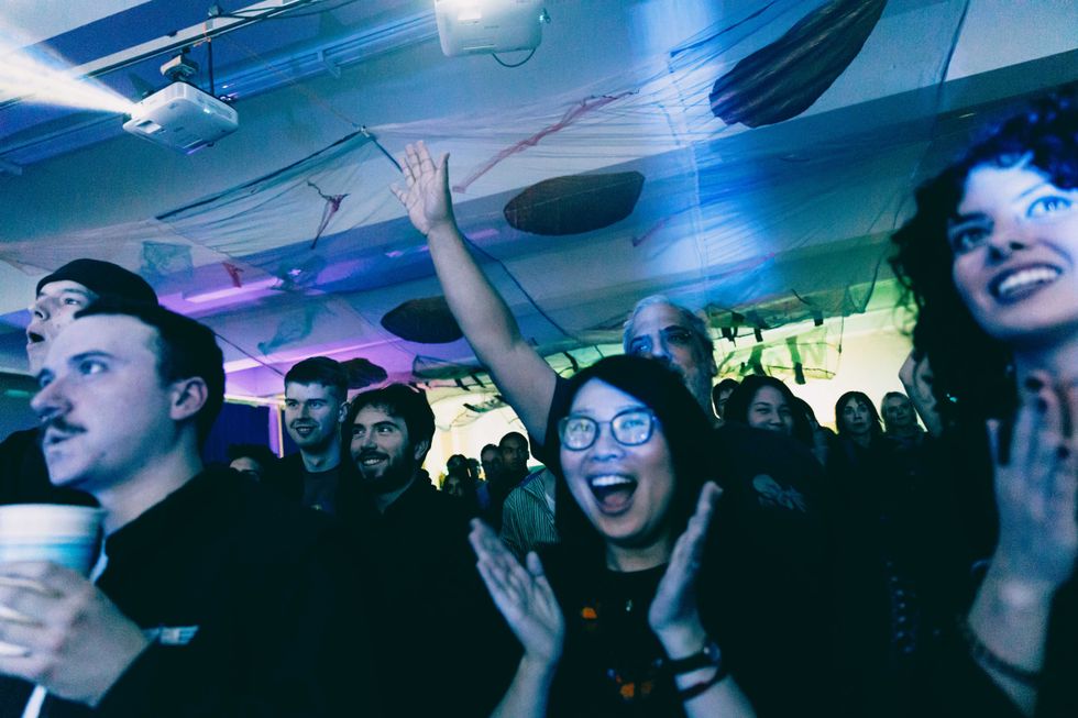 A woman smiles and claps her hands in a crowded concert audience.
