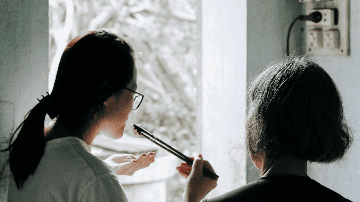 A younger asian woman uses chopsticks to taste a meal she cooks with an older relative