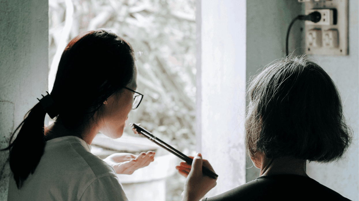 A younger asian woman uses chopsticks to taste a meal she cooks with an older relative