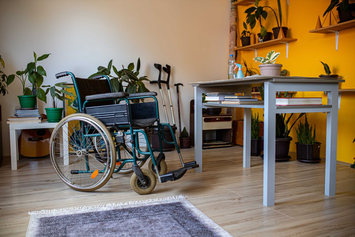 An empty wheelchair, crutches, and a walking stick in a cozy, plant-filled room