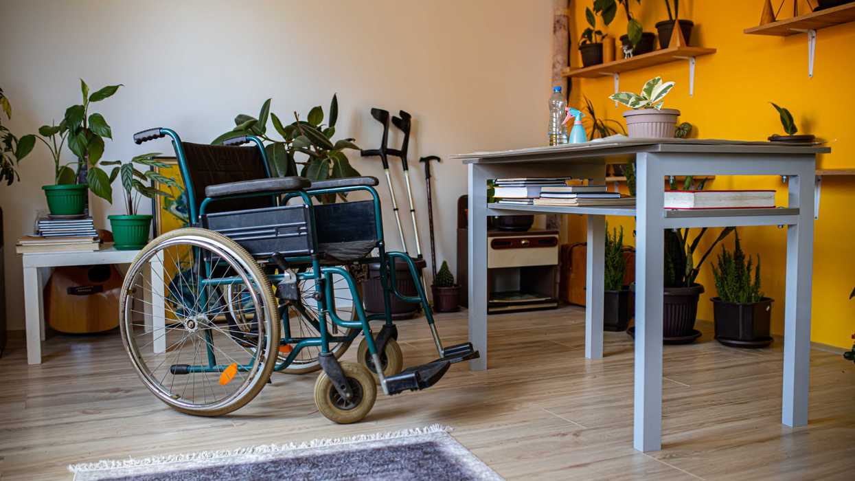 An empty wheelchair, crutches, and a walking stick in a cozy, plant-filled room