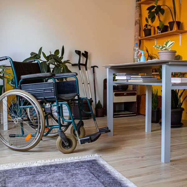 An empty wheelchair, crutches, and a walking stick in a cozy, plant-filled room