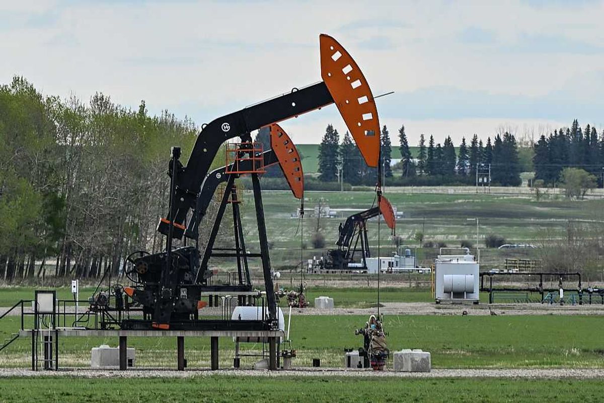 Black and orange oil pumpjacks in a green field under a cloudy sky