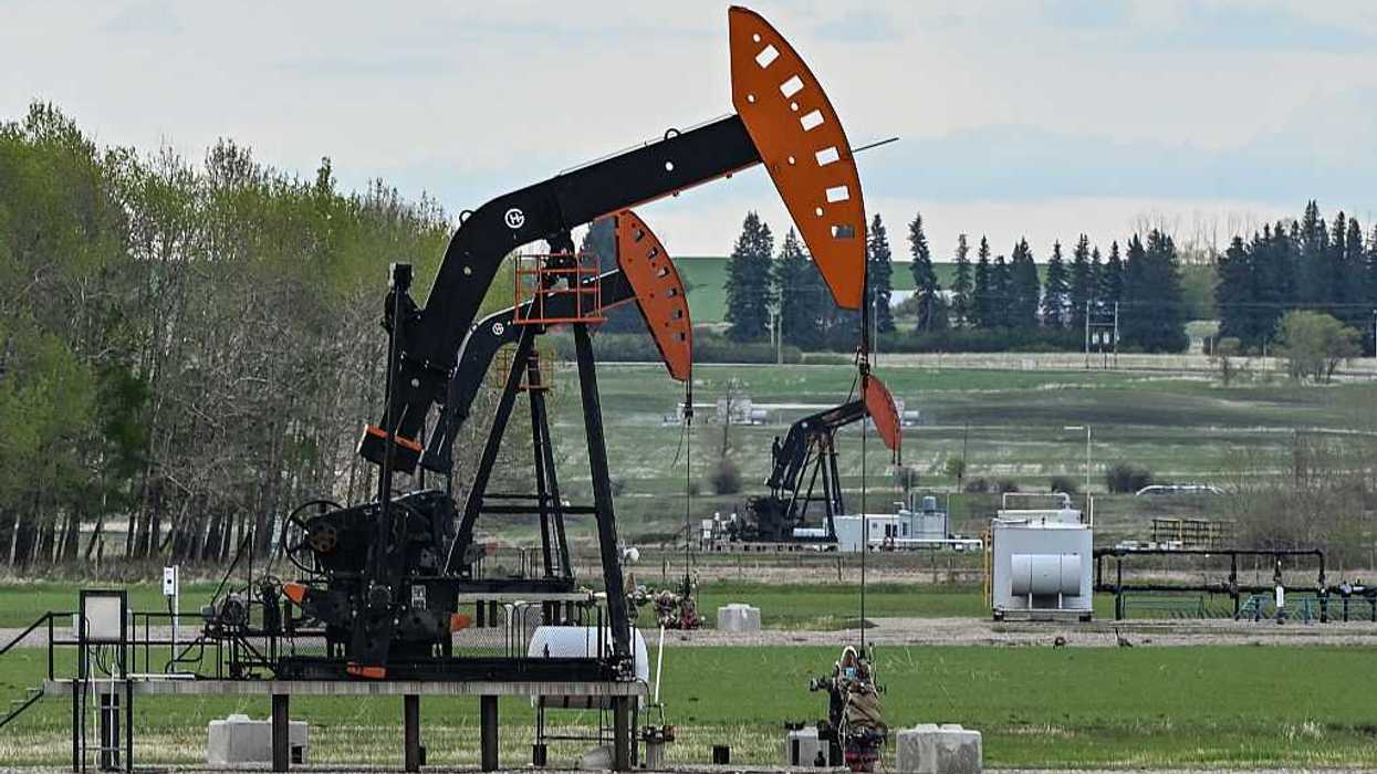 Black and orange oil pumpjacks in a green field under a cloudy sky