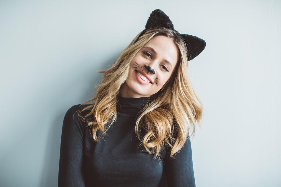 Blonde woman in a black cat costume, smiling, with cat ears and painted face.
