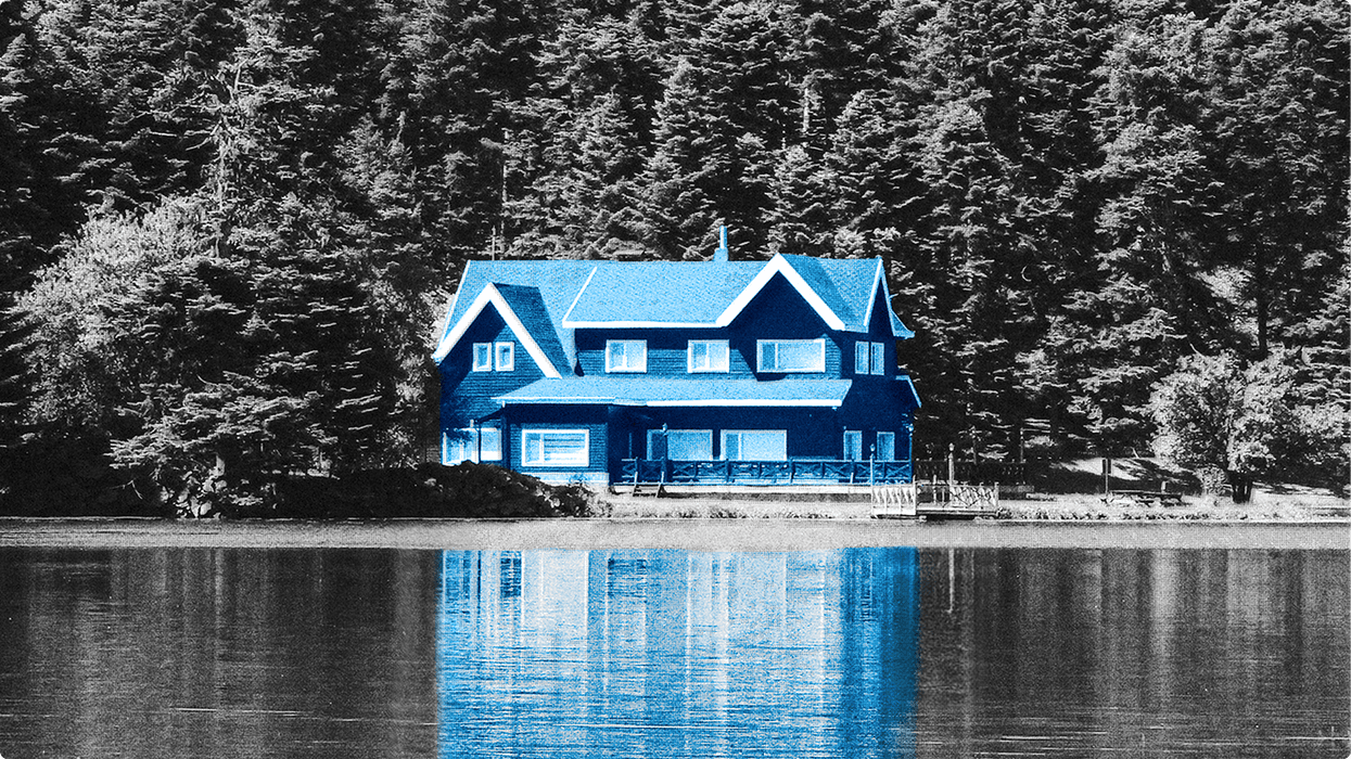 Blue house reflected in a lake, against a grayscale forest