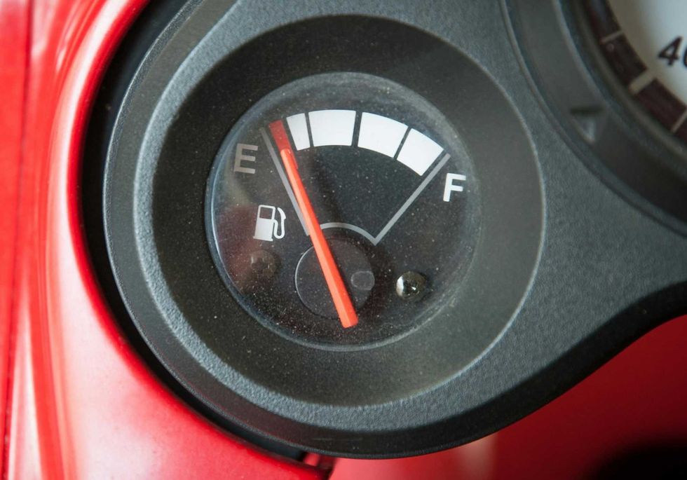 Close-up of a vehicle's fuel gauge with the red needle pointing to E for Empty, indicating low fuel