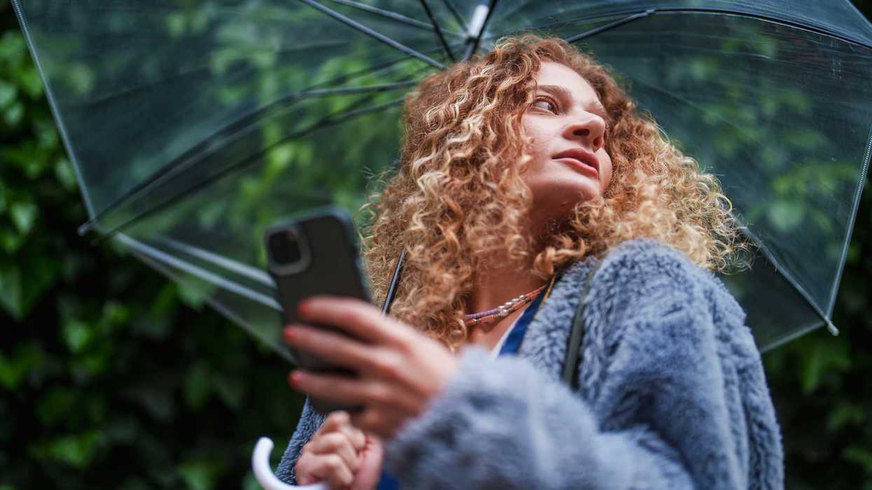 Curly-haired woman under clear umbrella holds phone, looking upwards