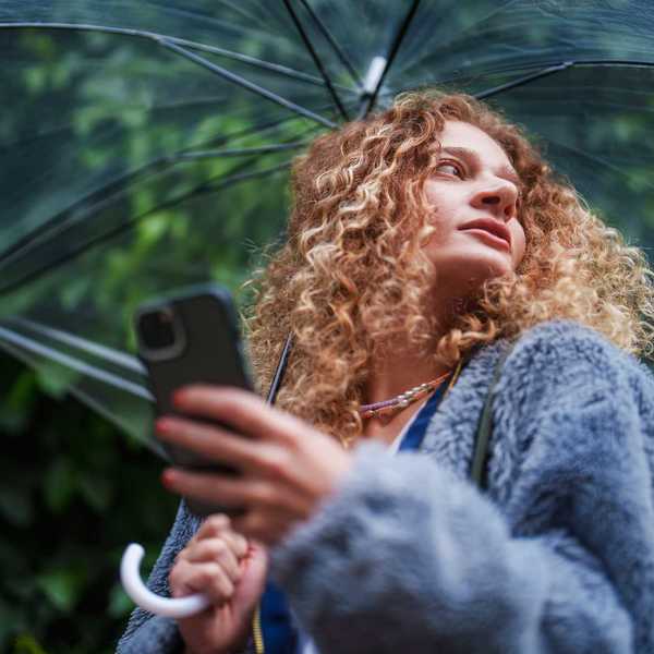 Curly-haired woman under clear umbrella holds phone, looking upwards
