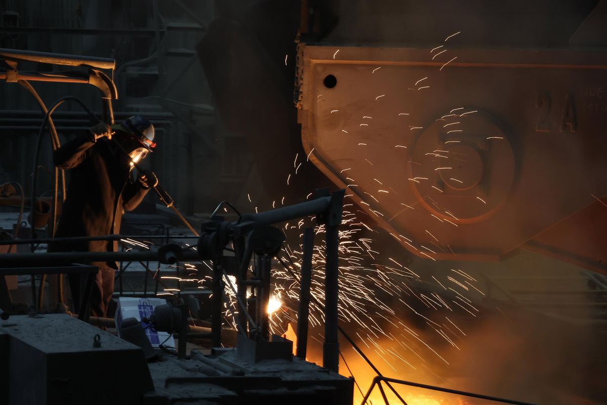 Foundry worker in protective gear operating a tool, sending bright sparks from molten metal.