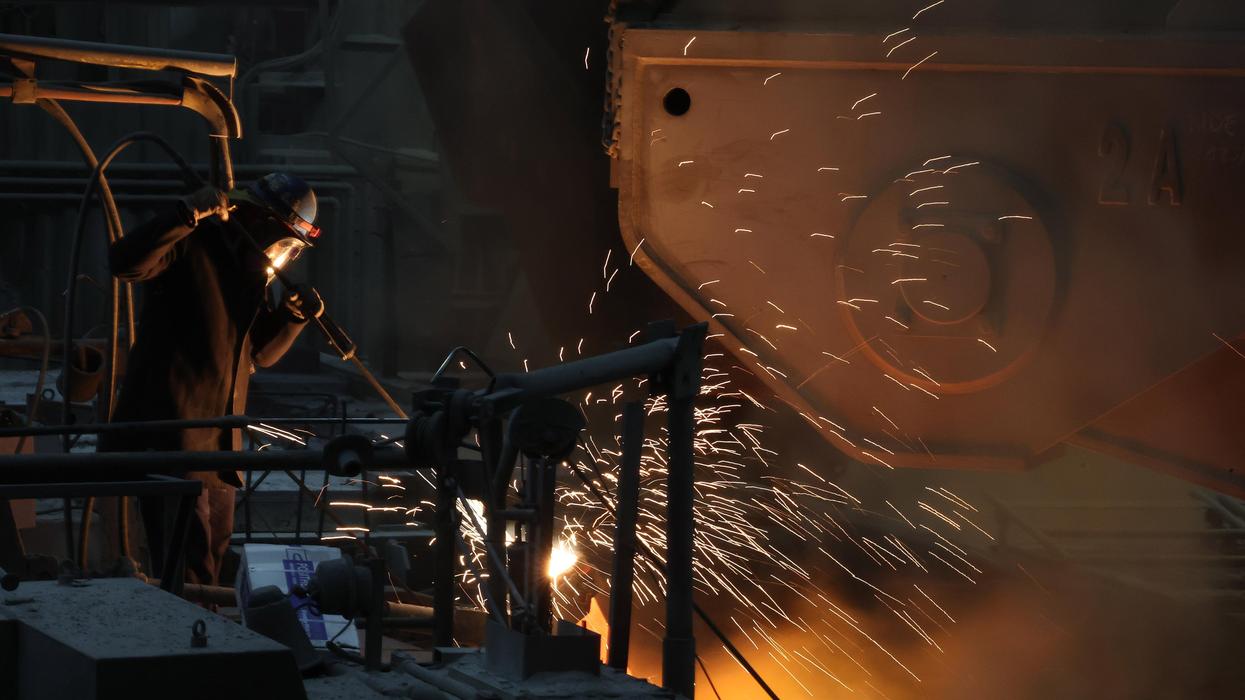 Foundry worker in protective gear operating a tool, sending bright sparks from molten metal.