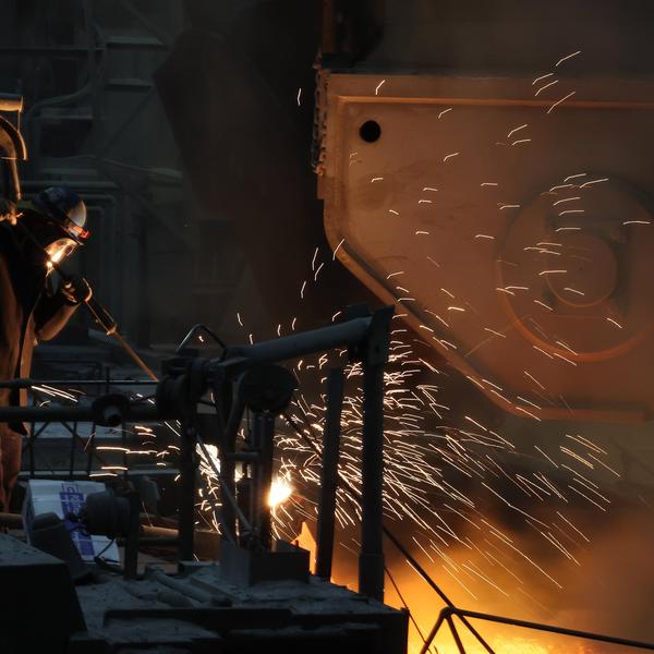 Foundry worker in protective gear operating a tool, sending bright sparks from molten metal.