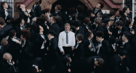 GIF of rapper Yung Lean smoking a cigarette while many dancers in private school uniforms dance around him