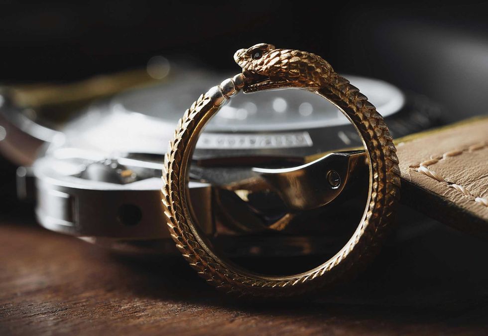 Gold Ouroboros snake ring biting its tail, blurred watch and strap in background