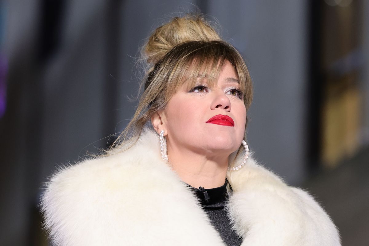 Kelly Clarkson wearing red lipstick, a messy bun, and a white fur coat, looking up
