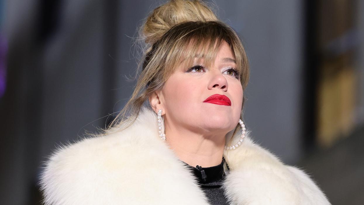 Kelly Clarkson wearing red lipstick, a messy bun, and a white fur coat, looking up