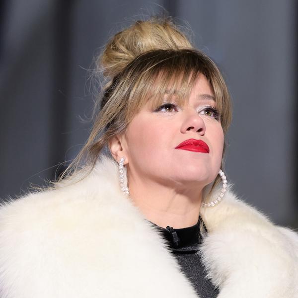 Kelly Clarkson wearing red lipstick, a messy bun, and a white fur coat, looking up