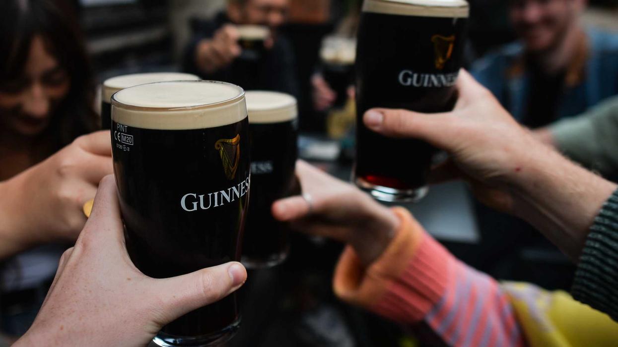 Multiple hands holding and clinking dark Guinness pints with creamy white heads
