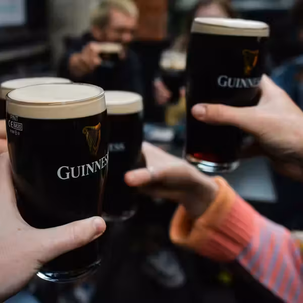 Multiple hands holding and clinking dark Guinness pints with creamy white heads