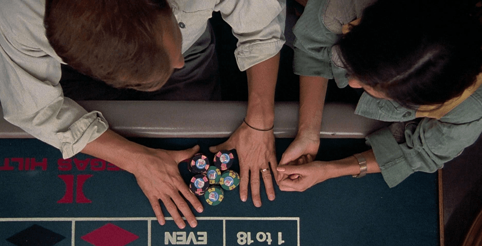 Overhead view of two people placing casino chips on a blue betting table at a Vegas casino.