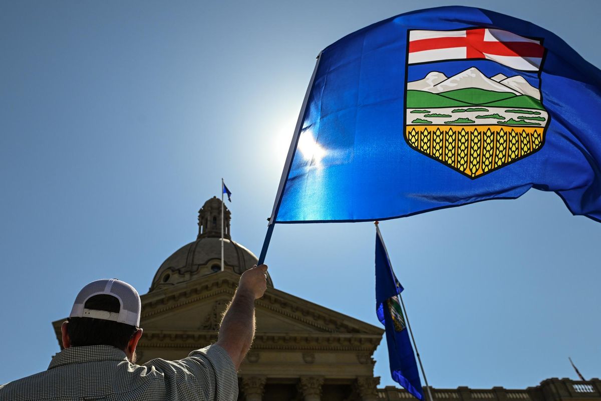 Person holds large Alberta flag against sunny sky