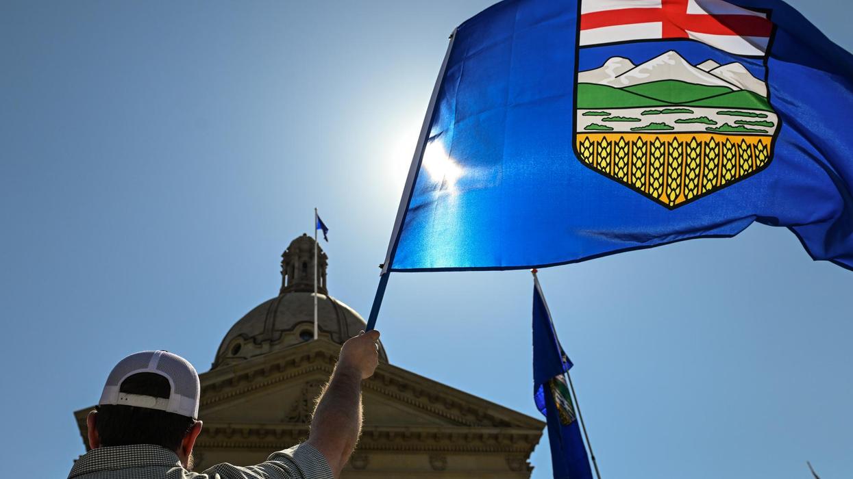 Person holds large Alberta flag against sunny sky