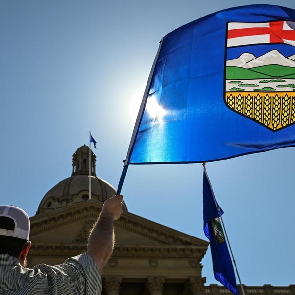 Person holds large Alberta flag against sunny sky