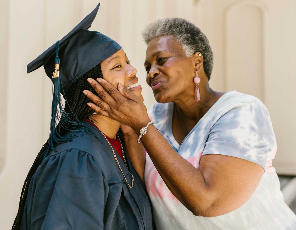Proud older woman affectionately holds the face of a smiling graduate in cap and gown