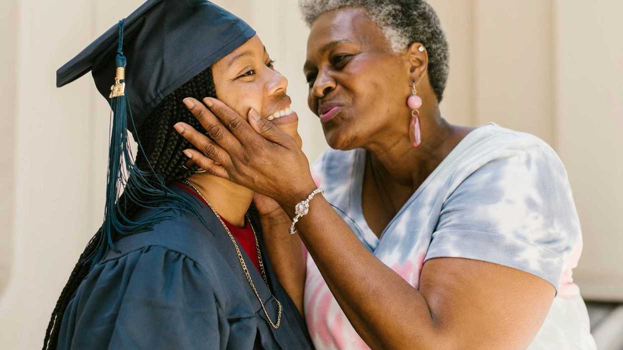 Proud older woman affectionately holds the face of a smiling graduate in cap and gown