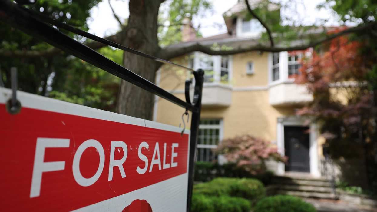 Red For Sale sign in foreground, yellow house blurred in background