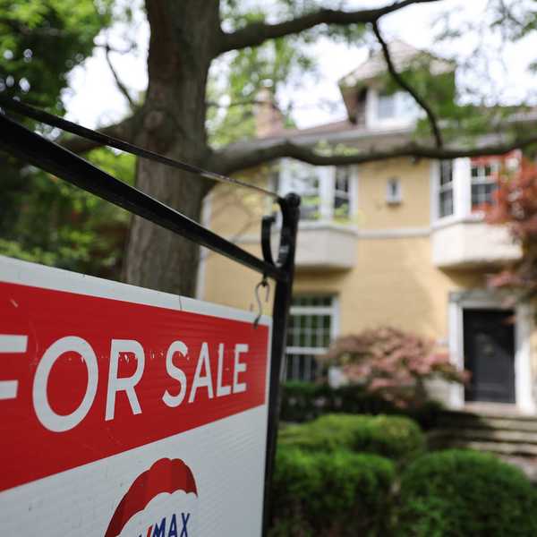 Red For Sale sign in foreground, yellow house blurred in background