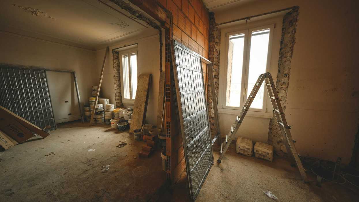 Room under renovation, exposed brick wall, ladder, paint buckets, and building materials.
