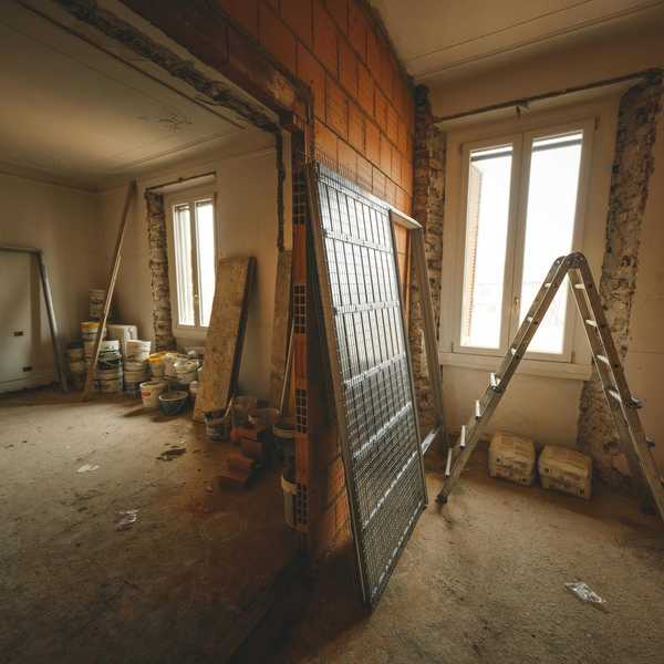 Room under renovation, exposed brick wall, ladder, paint buckets, and building materials.
